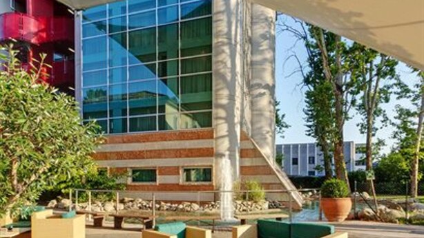 Un área de estar al aire libre con muebles modernos, una jardinera grande y un edificio con ventanas de vidrio reflectante al fondo.