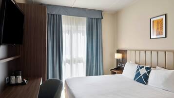 A hotel room with a bed, a desk, a chair, a television, a nightstand, a lamp, and a framed picture on the wall.
