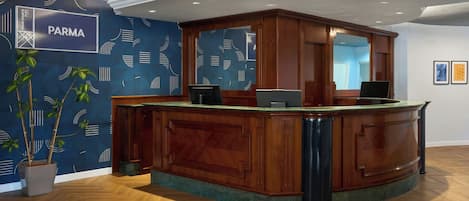A reception desk with a wooden finish, a blue patterned wall, and a potted plant.