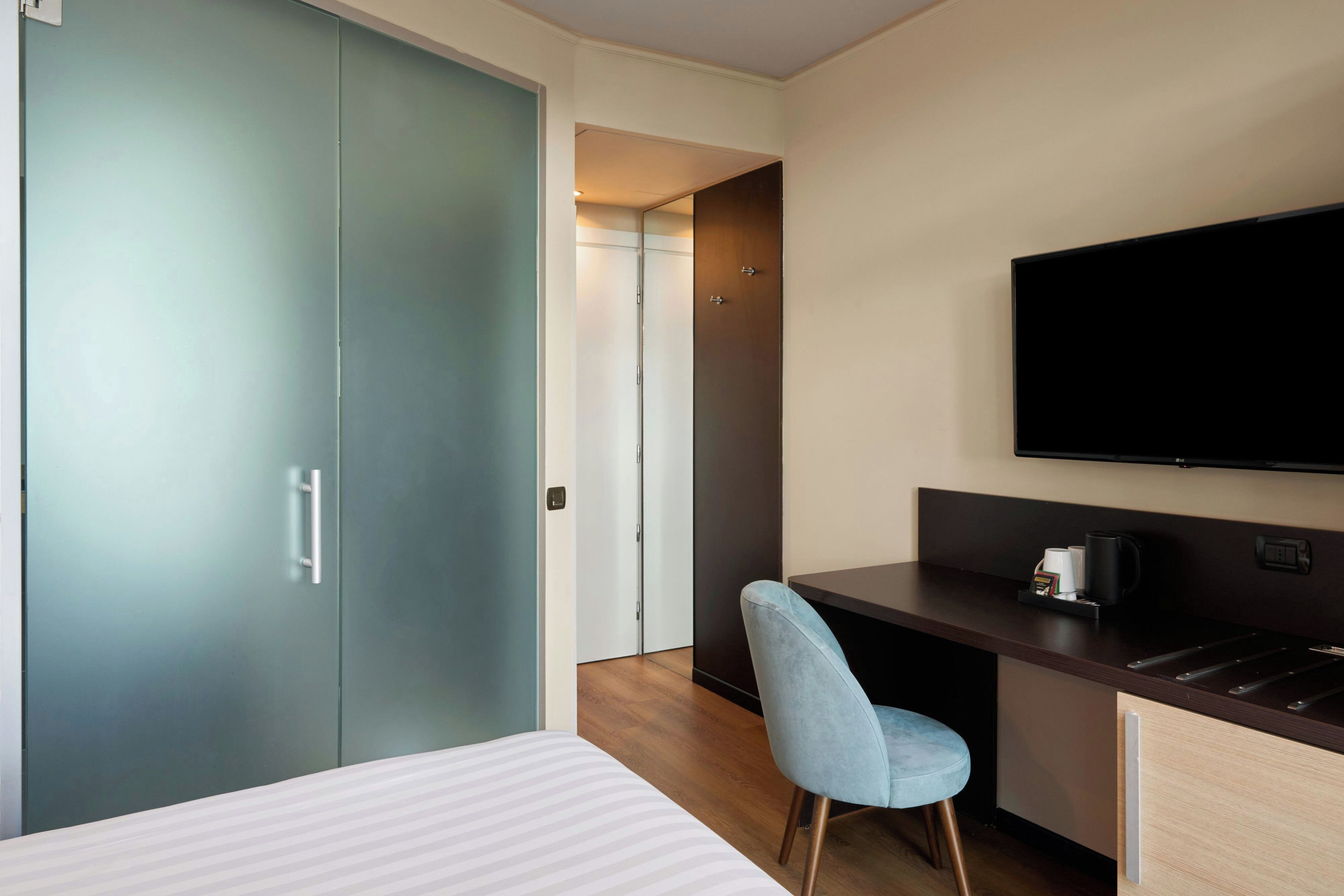Una habitación de hotel con una cama, un escritorio con una silla, un televisor y un armario.