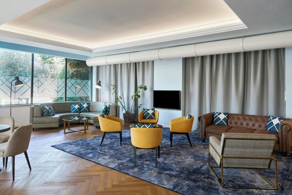 A modern living room with a sofa, armchairs, a coffee table, and a TV. - Four Points Flex by Sheraton Parma (Parma)