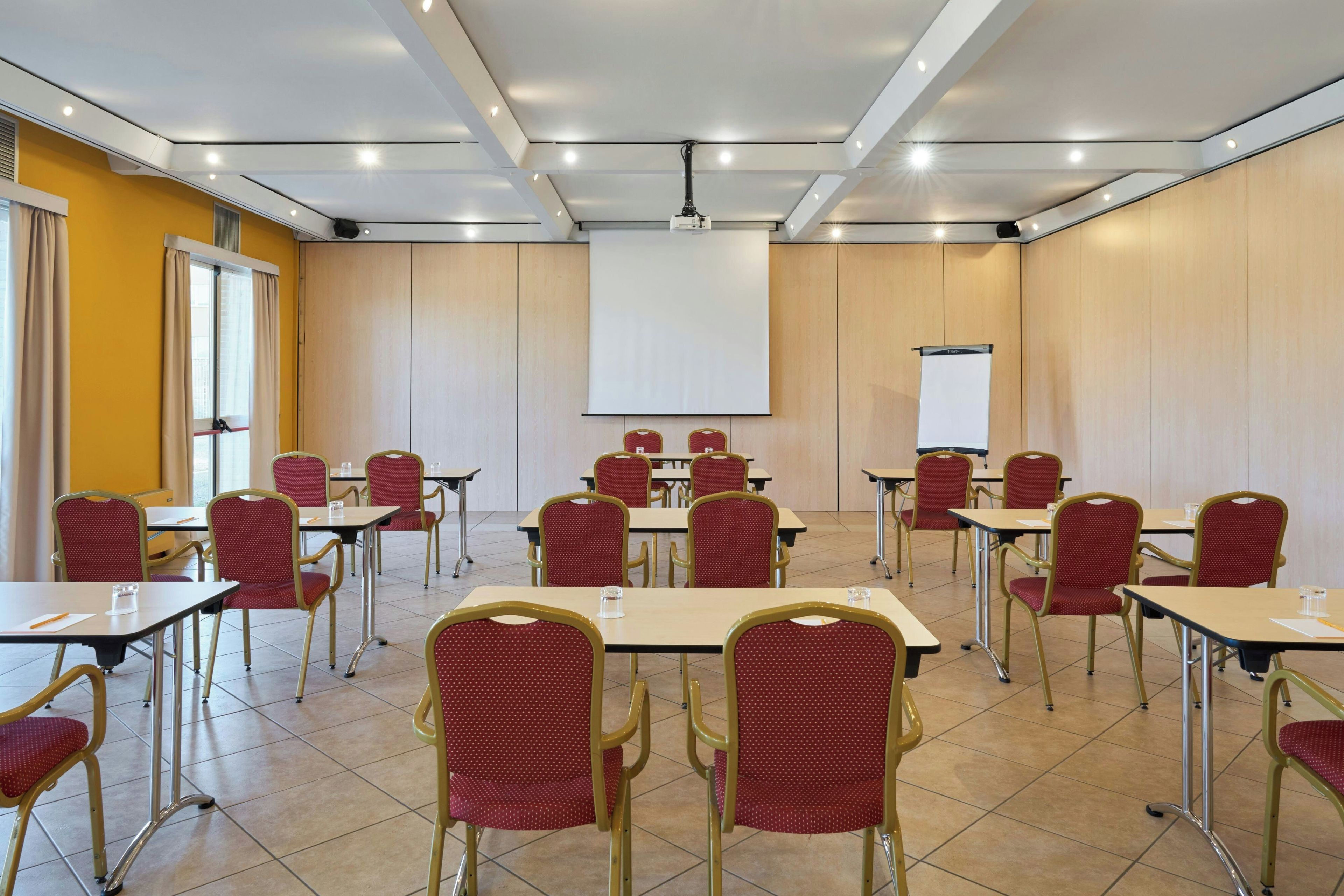 A conference room with tables and chairs, a projector screen, and a whiteboard.