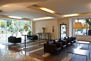 A hotel lobby with a reception desk, seating area, and large windows offering views of the outdoors.