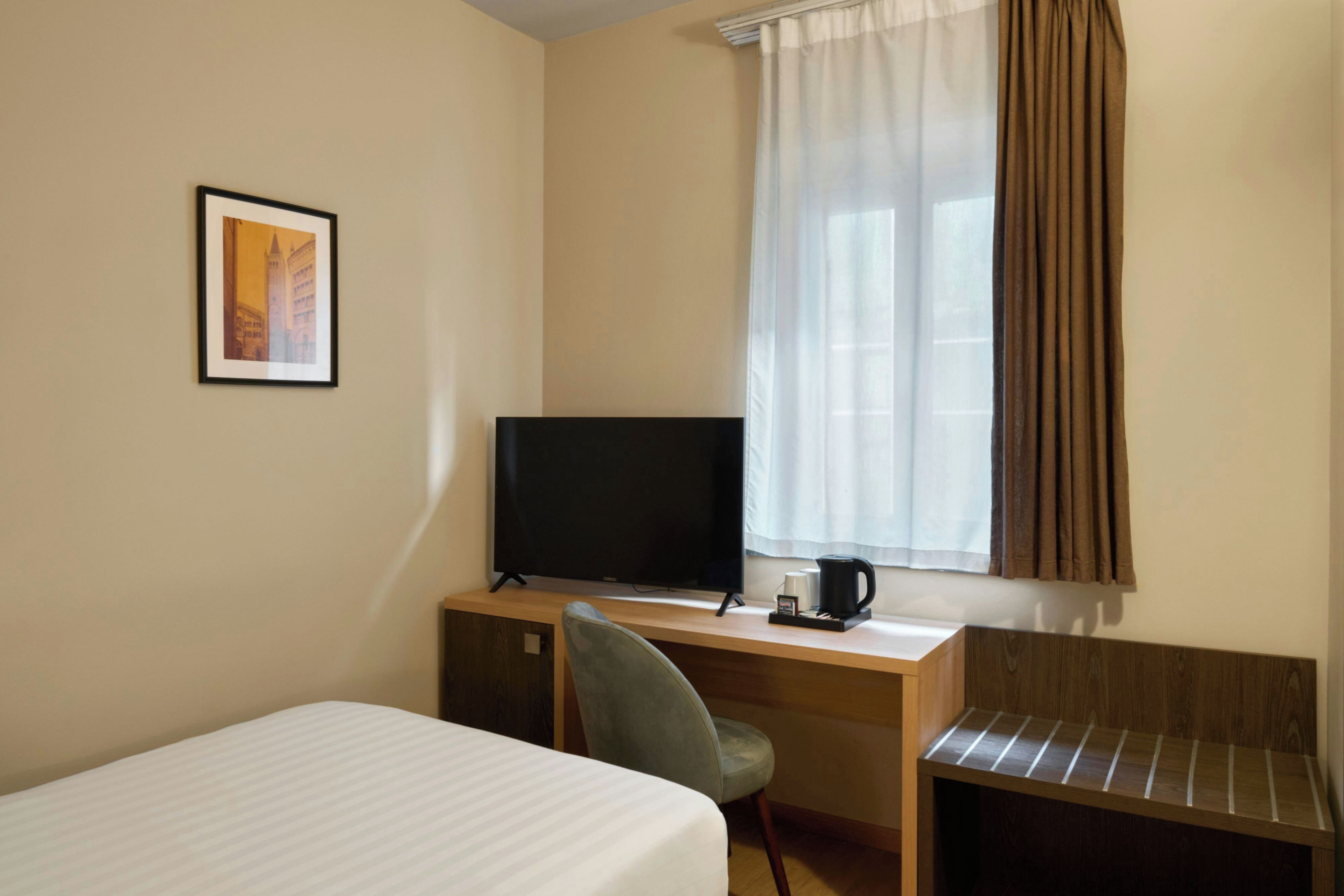 A hotel room with a bed, a desk with a television, a chair, and a window with curtains.