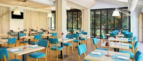 Un comedor amplio con varias mesas y sillas, ventanas grandes con vistas a zonas verdes, e iluminación moderna.
