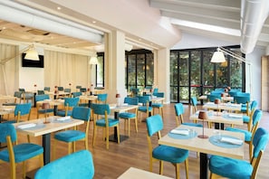 Un comedor amplio con varias mesas y sillas, ventanas grandes con vistas a zonas verdes, e iluminación moderna.