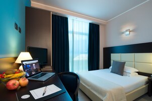 A hotel room with a bed, desk, laptop, fruits, and a TV.