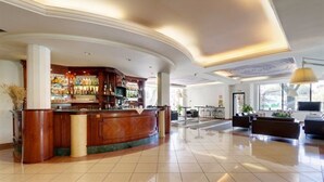 Un vestíbulo espacioso con un mostrador de recepción curvo, una zona de bar y un área de estar con un amplio ventanal que ofrece vistas al exterior.