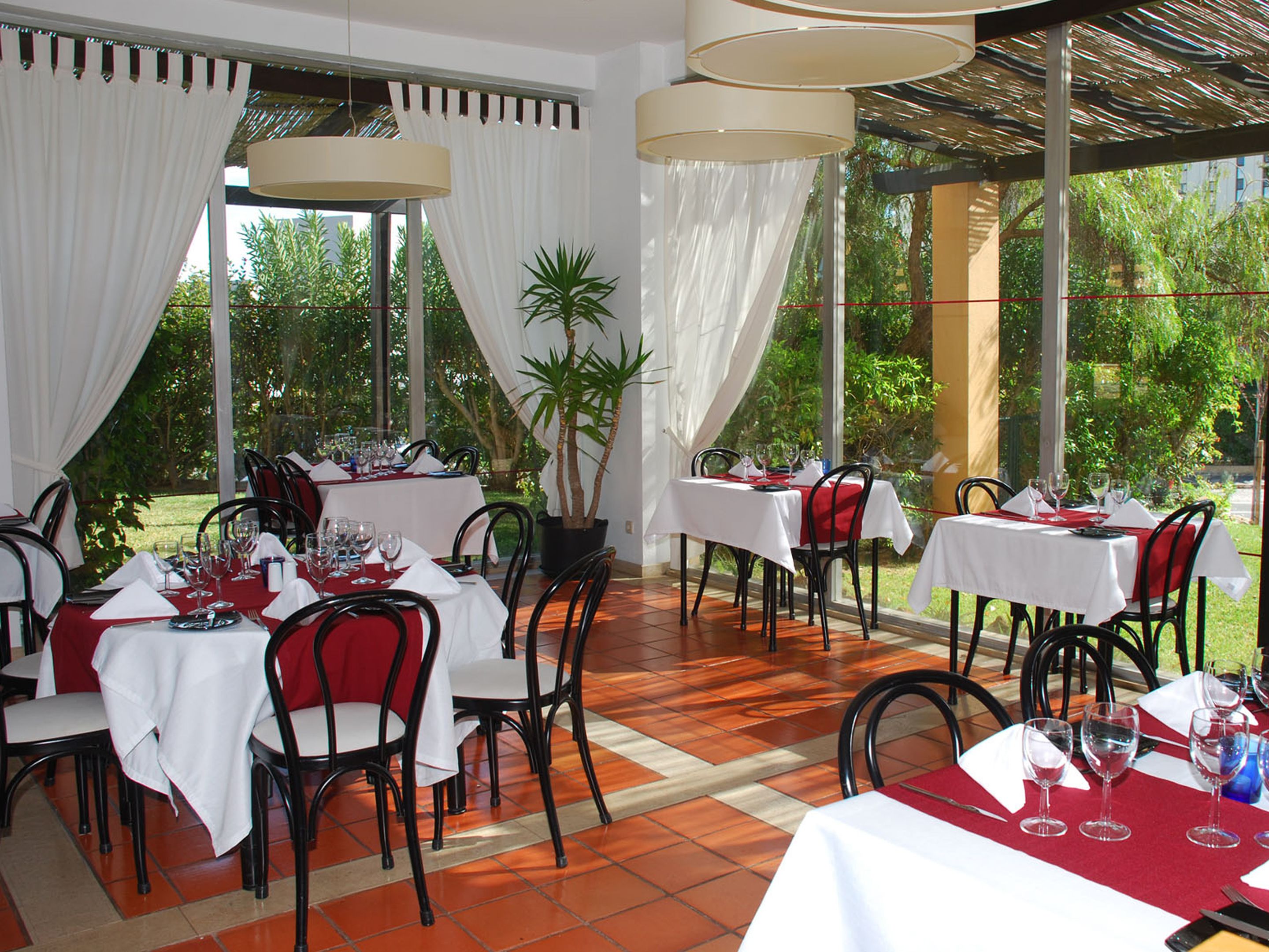 An outdoor dining area with tables set for two, featuring white tablecloths and red napkins.