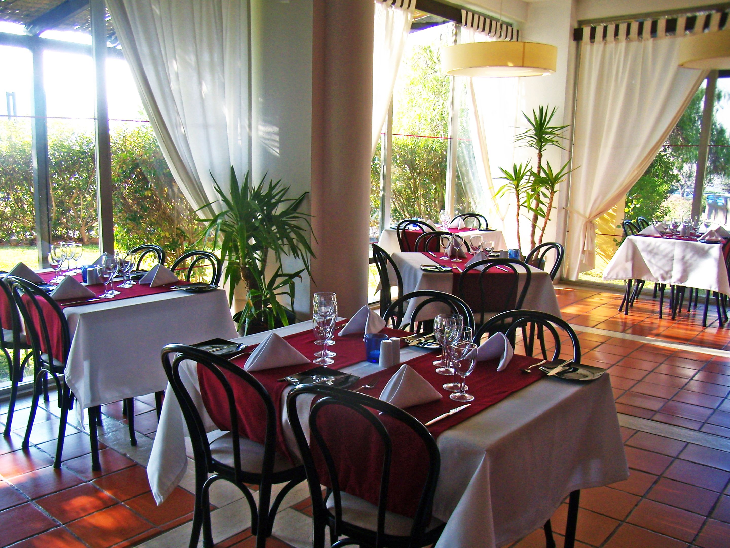 A restaurant with tables set for dining, chairs, and potted plants.