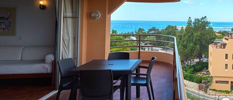 A balcony with a table and chairs, a sofa, and a view of the sea.