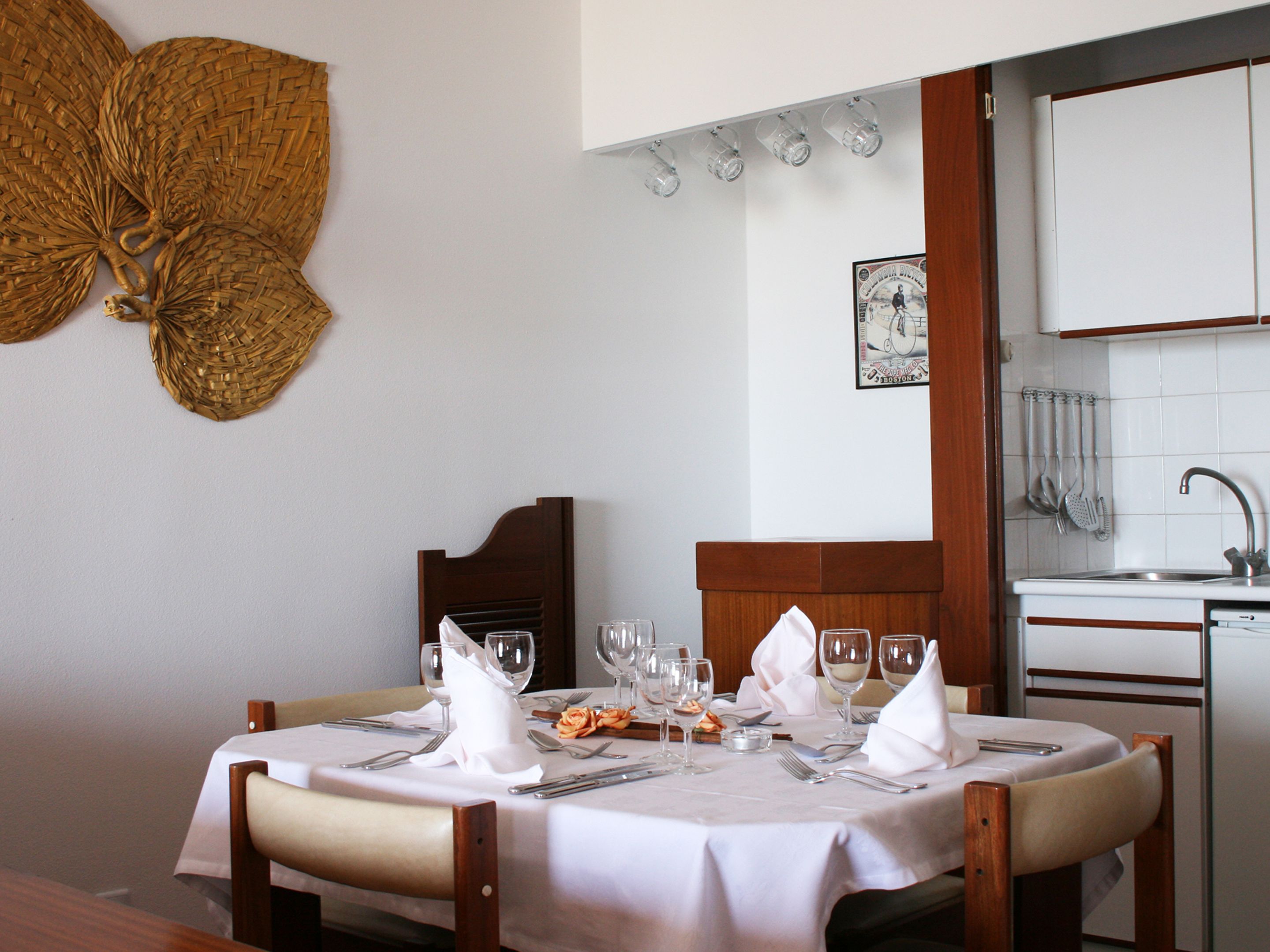 A dining area with a table set for two, a kitchen with white cabinets, and a decorative wall piece.