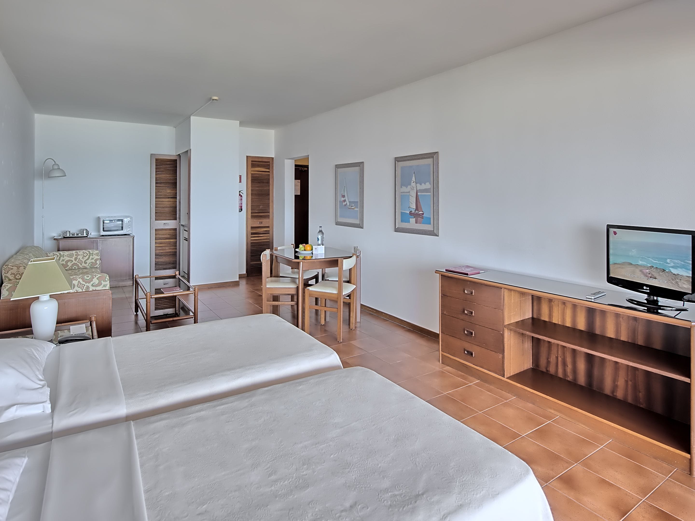 A hotel room with two beds, a desk, a television, and a dining area.