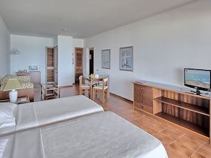 A hotel room with two beds, a desk, a television, and a dining area.
