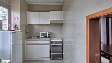 Una cocina compacta con armarios blancos, un microondas, una estufa y un lavamanos.