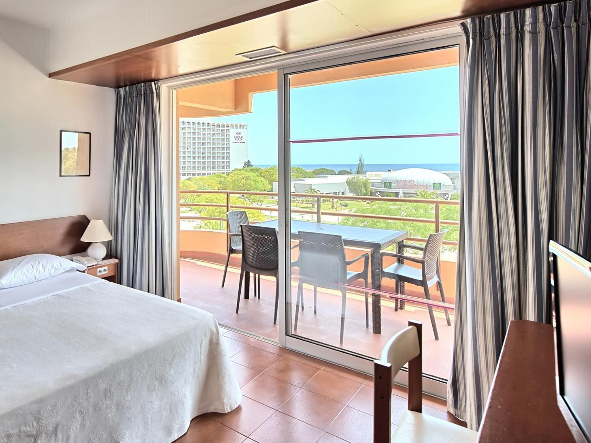 A hotel room with a bed, a desk, and a view of a casino and greenery.