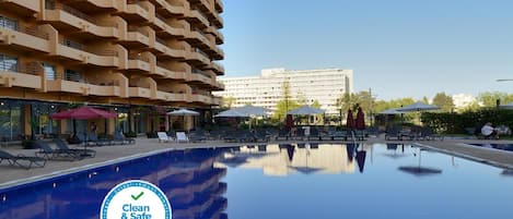 Un hôtel moderne doté d’une grande piscine, de chaises longues et d’un espace salon extérieur.