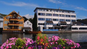 Un hôtel situé au bord de l’eau, avec un bâtiment moderne, une maison jaune de style traditionnel et un bateau amarré à proximité.
