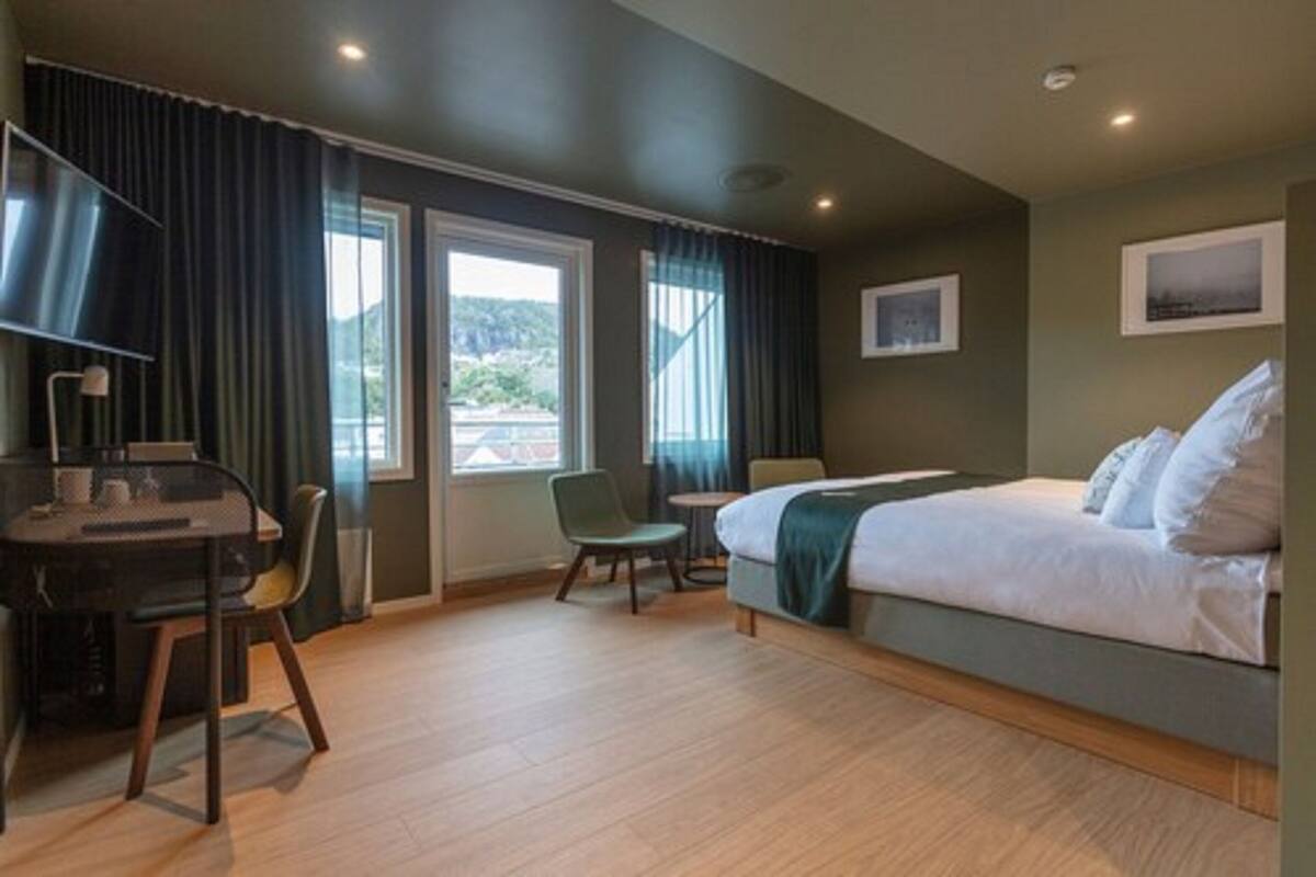Une chambre d’hôtel avec un lit, un bureau, une chaise et une fenêtre avec des rideaux.