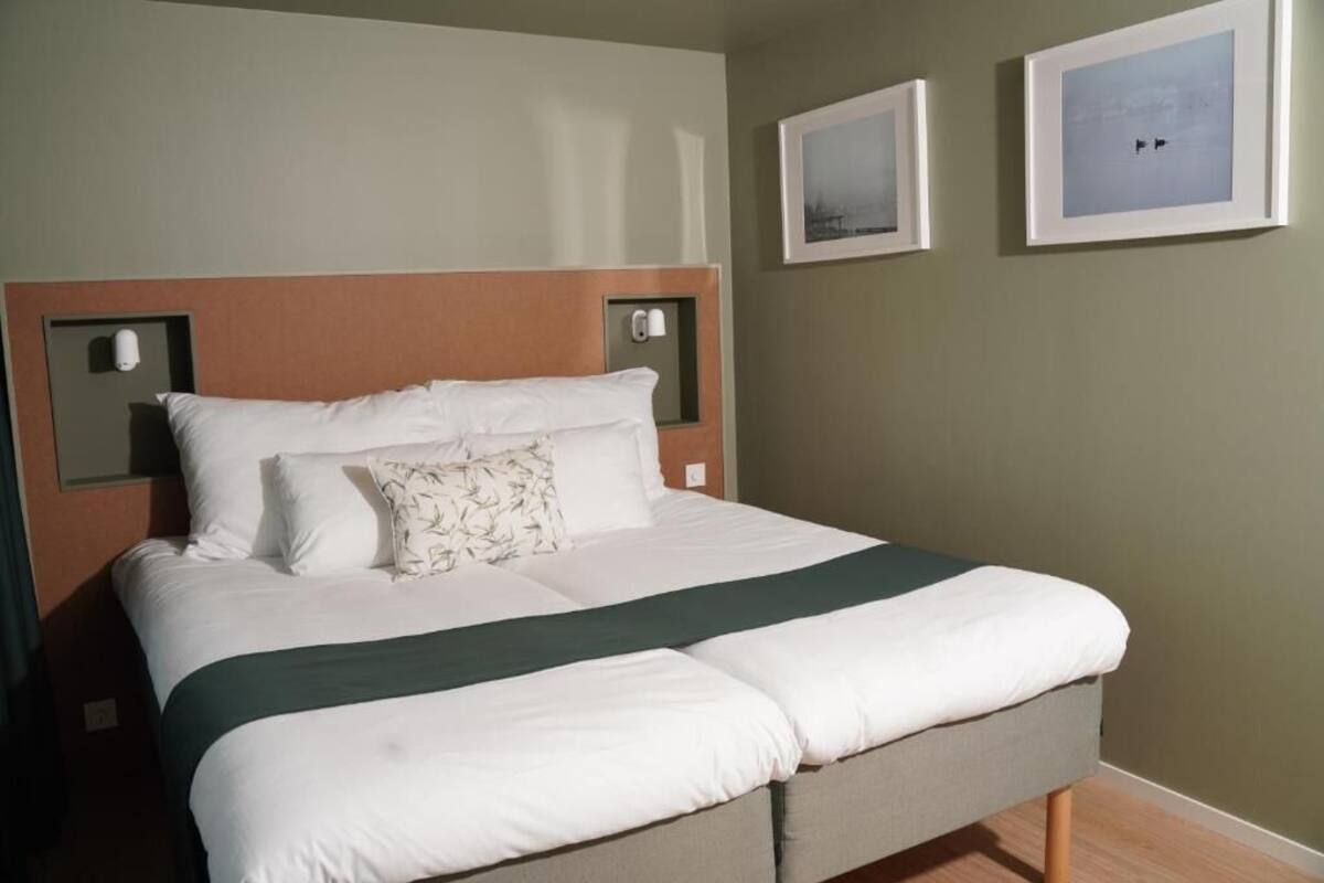 Un lit bien fait, avec une tête de lit, une table de chevet et deux tableaux encadrés accrochés au mur.