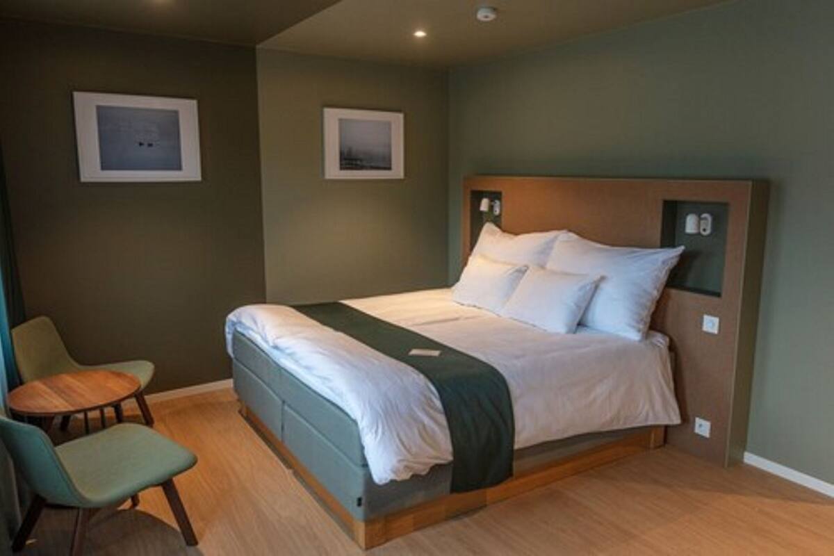 Un lit simple avec une tête de lit en bois, une table de chevet et deux chaises.