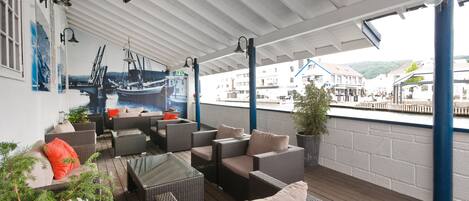 A covered outdoor seating area with wicker furniture and a view of boats in the background.