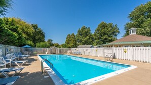 Una piscina rettangolare con interno blu, circondata da recinzioni bianche e alberi all'ombra.