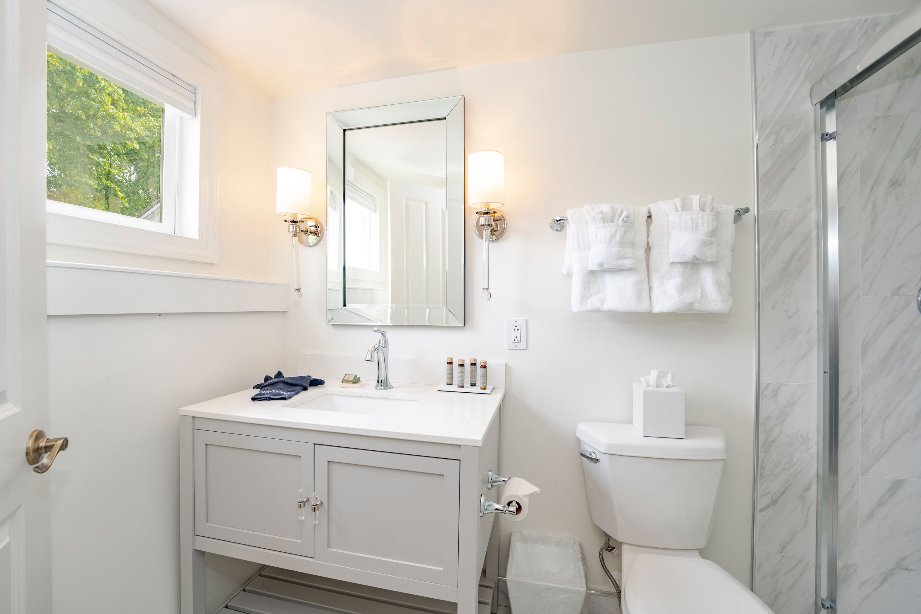 A bathroom with a white vanity, a large mirror, two wall-mounted lights, a toilet, and a glass shower enclosure.