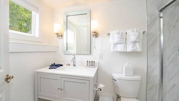 A bathroom with a white vanity, a large mirror, two wall-mounted lights, a toilet, and a glass shower enclosure.