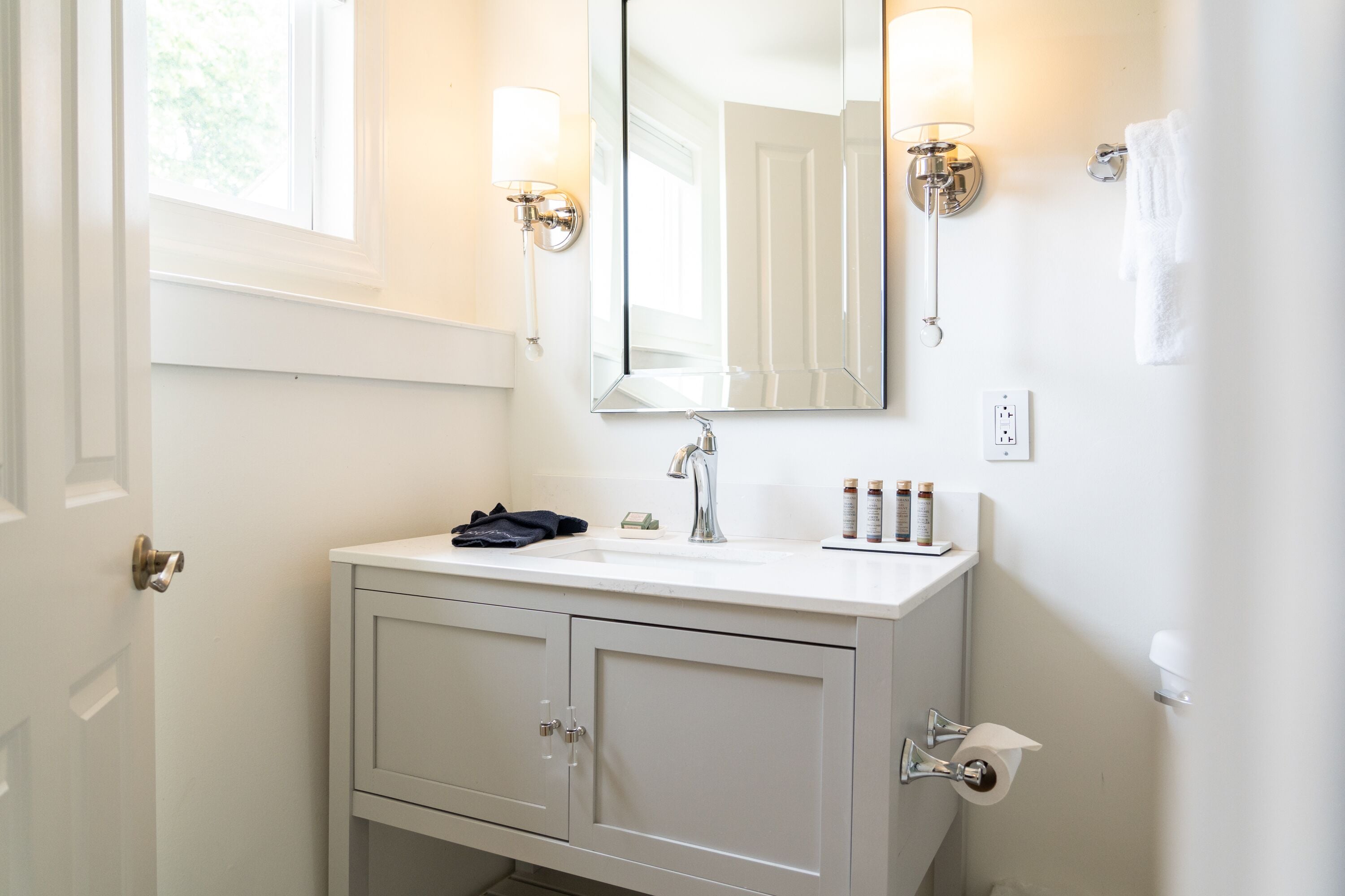 A bathroom with a white vanity, a mirror, a sink, and two wall-mounted lights.