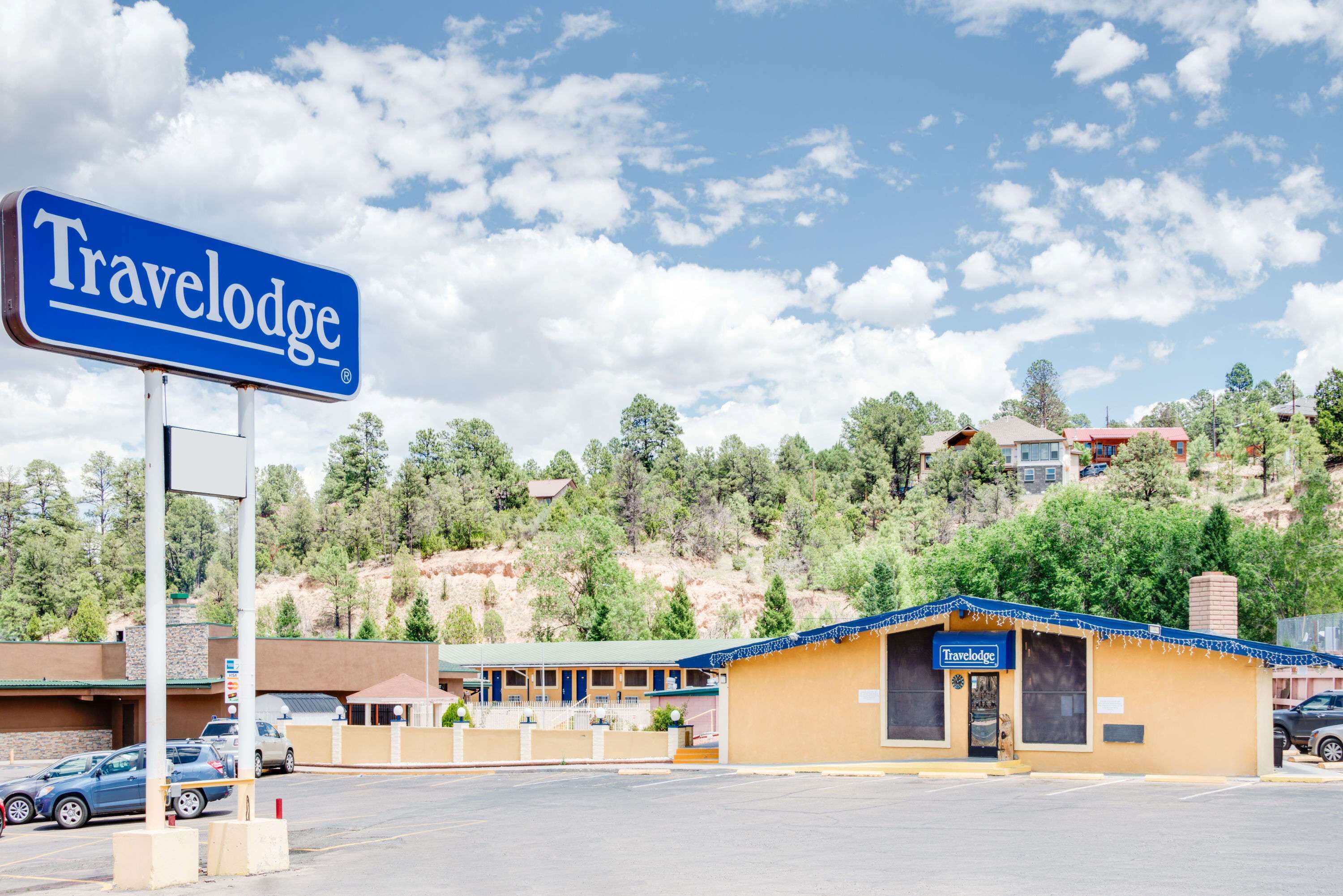 Un hôtel Travelodge avec une enseigne bleue, un parking et un paysage montagneux en arrière-plan.