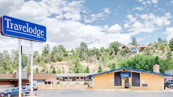 Un hotel Travelodge con un letrero azul, un estacionamiento y montañas al fondo.