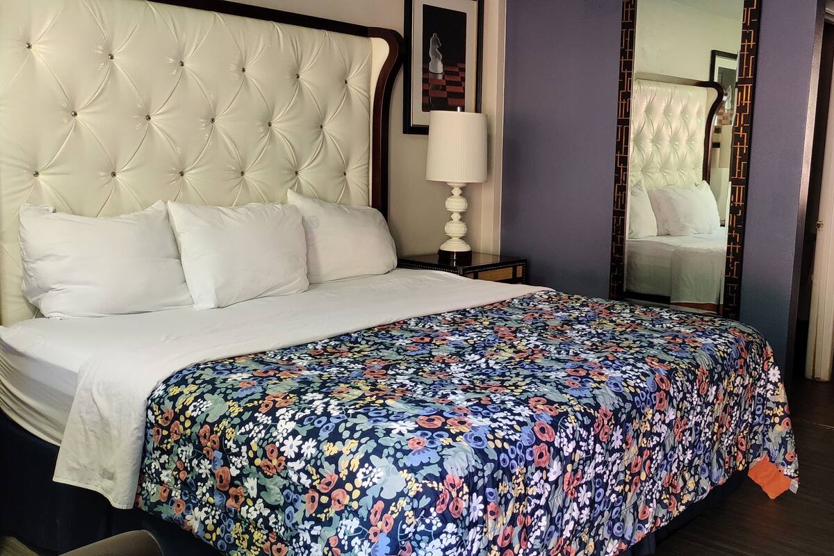 Une chambre d’hôtel avec un grand lit, une table de chevet avec une lampe, une commode et un miroir.