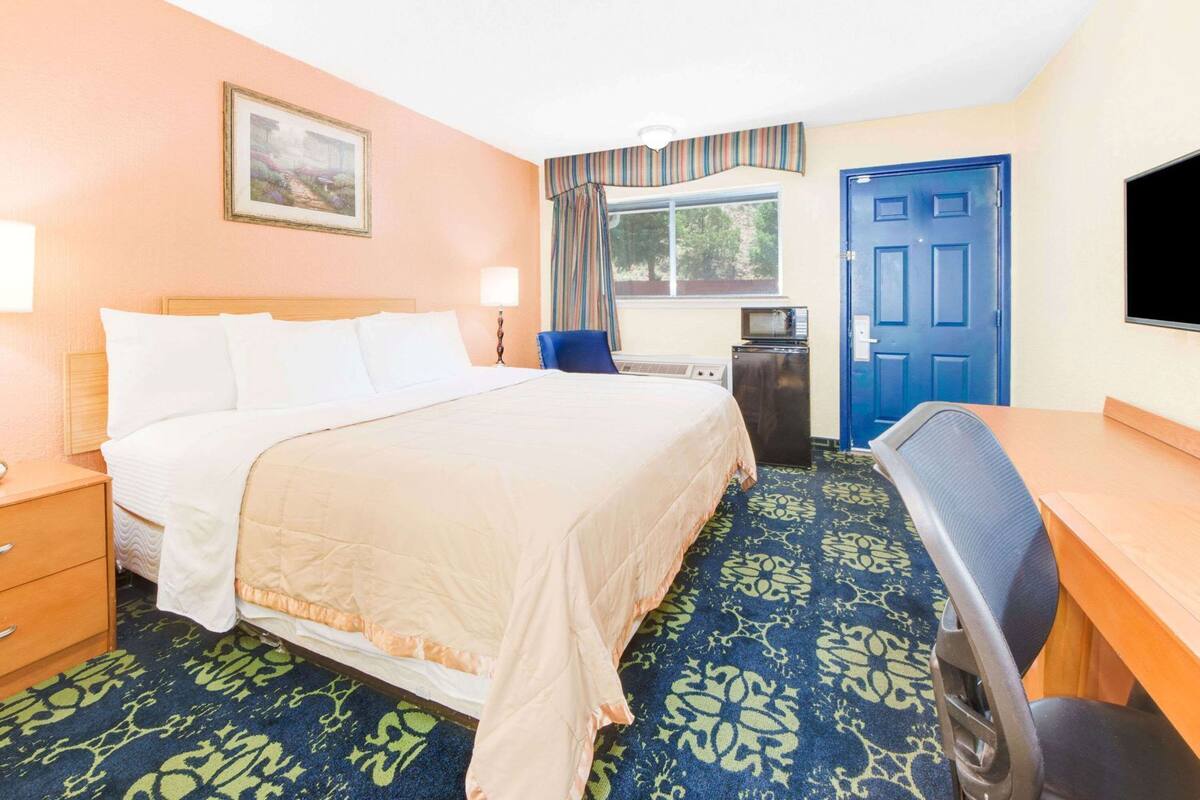 Une chambre d’hôtel équipée d’un lit, d’un bureau, d’une chaise, d’une télévision et d’une fenêtre avec des rideaux.