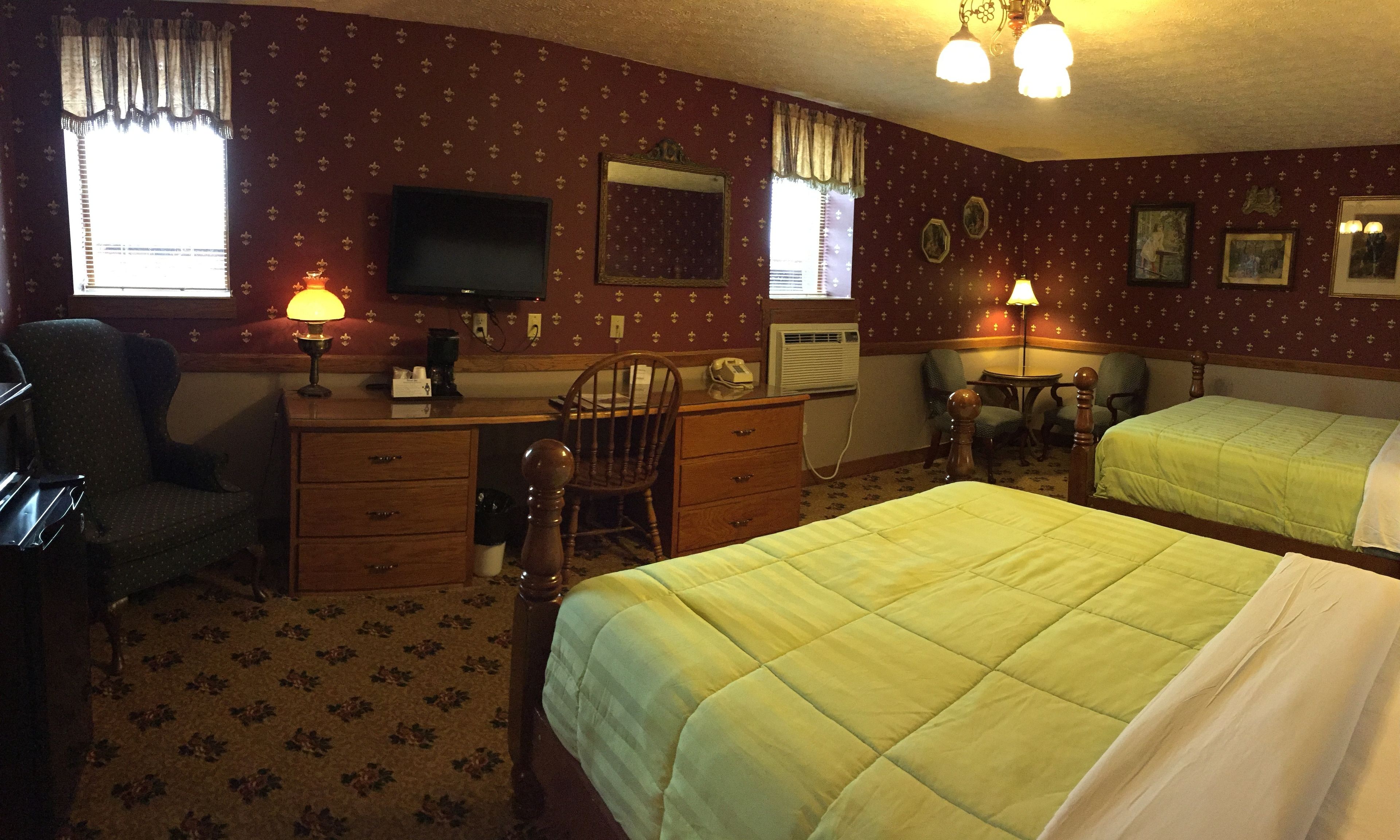 A hotel room with two beds, a desk, a chair, a television, and a window with curtains.