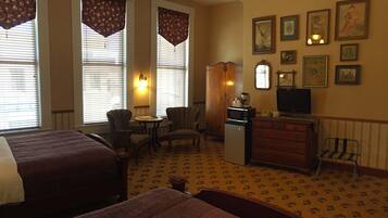 Quarto de hotel com duas camas, uma escrivaninha com computador, uma cadeira, um pequeno frigorífico e uma televisão.