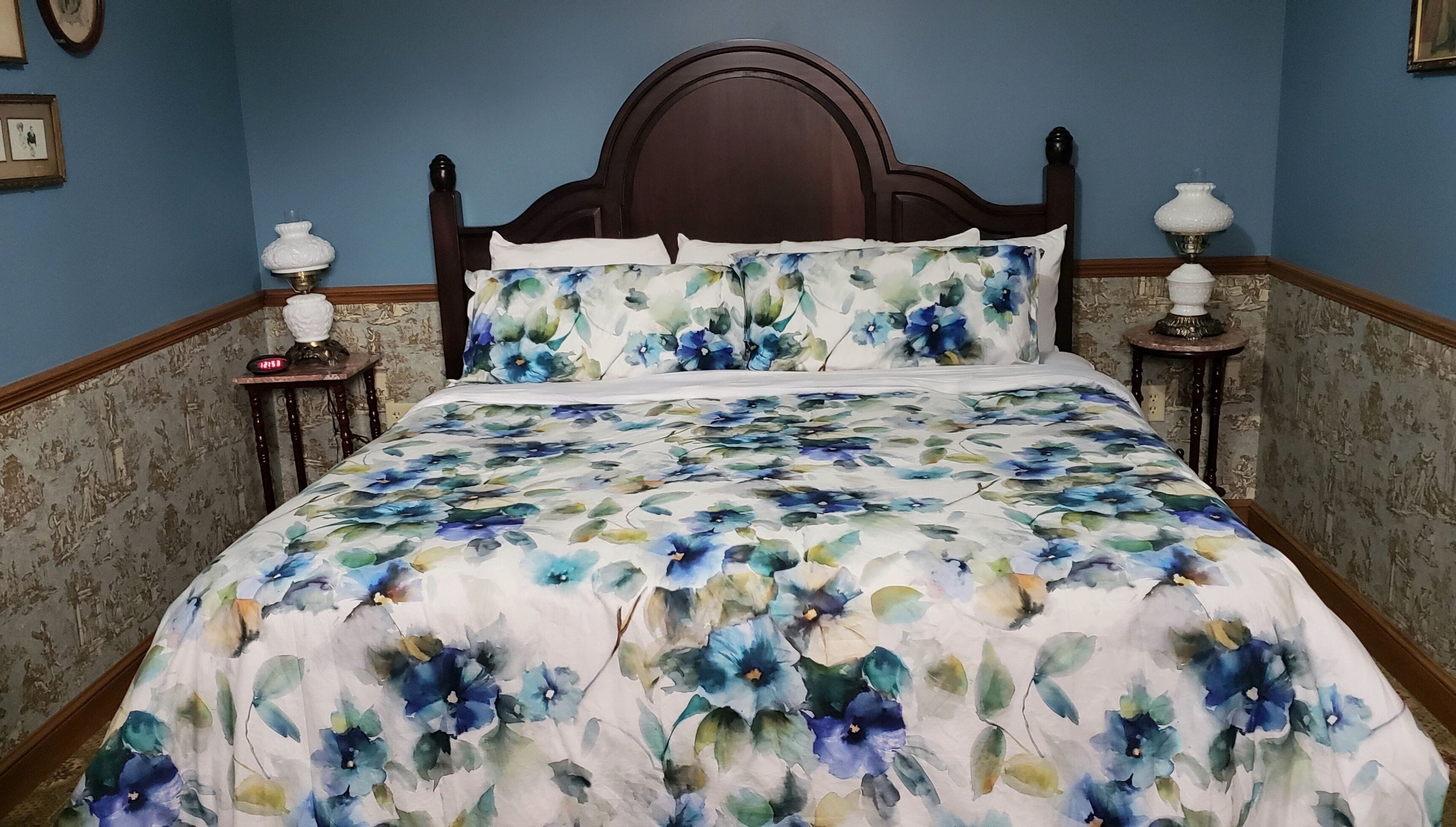 Un dormitorio con colcha estampada, cabecera de madera, dos lámparas de noche y papel tapiz decorado.