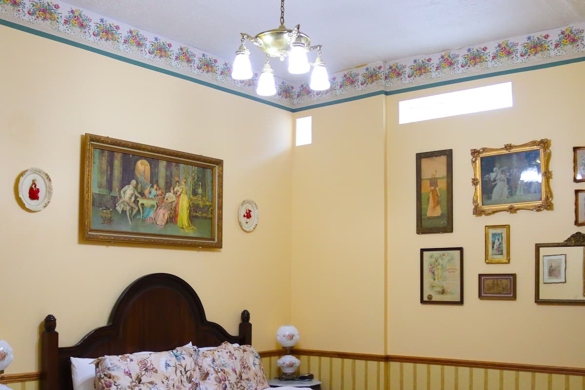 Ein Schlafzimmer mit floralem Bettbezug, einem Holzkopfteil, einem Nachttisch mit Lampe und einem Gemälde an der Wand.