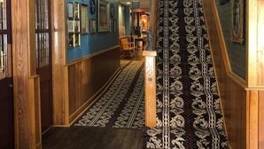 Um corredor com painéis de madeira, carpete estampado e escada que leva a um andar superior.