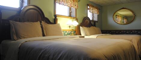 A room with two beds, a mirror, and a window with floral curtains.