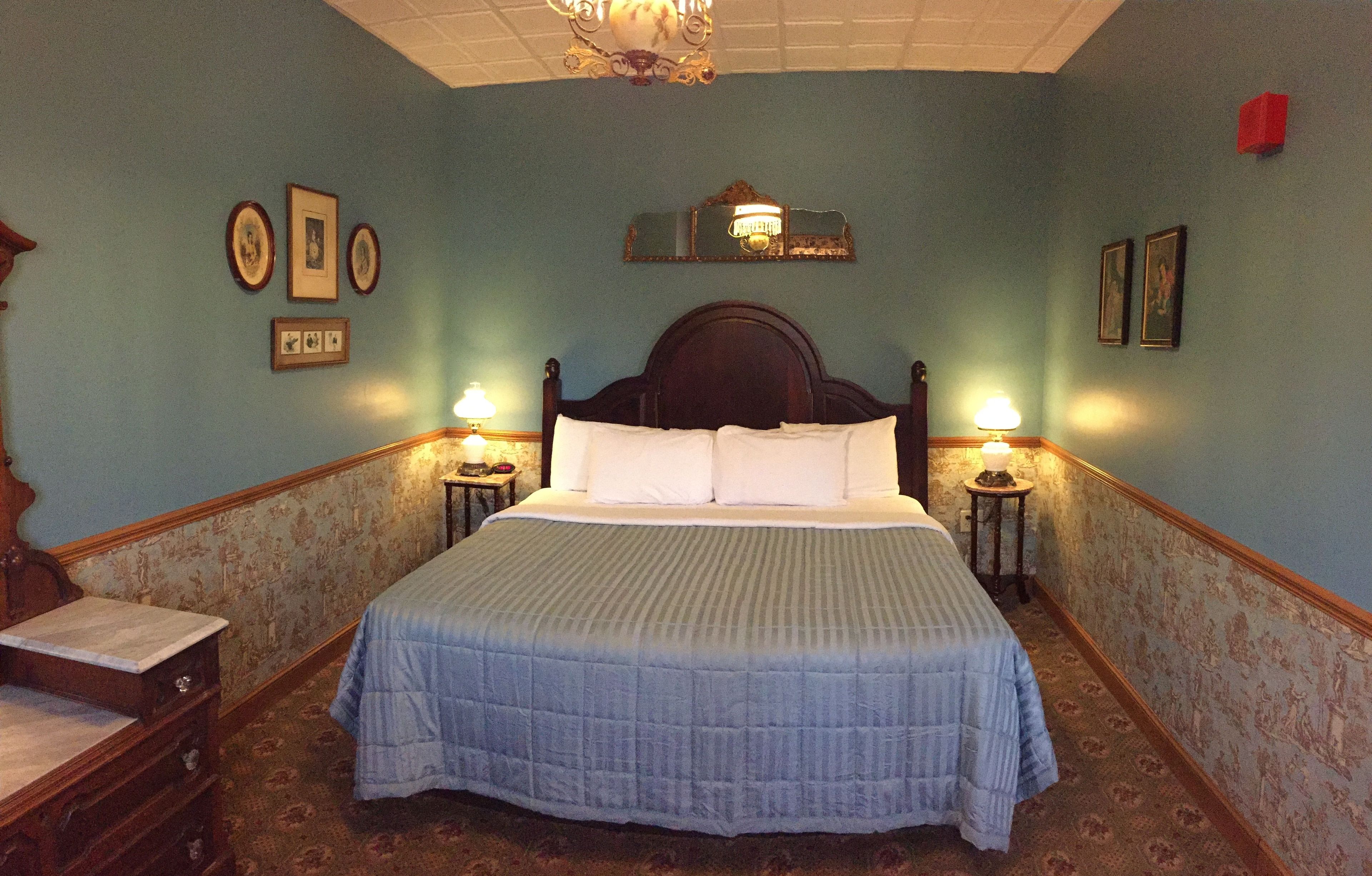 A bedroom with a large bed, two bedside tables with lamps, a dresser, and framed pictures on the walls.