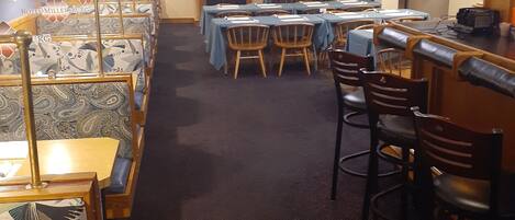 Un espace de restauration d’hôtel comprenant des banquettes et des tables, une cheminée et un bar.