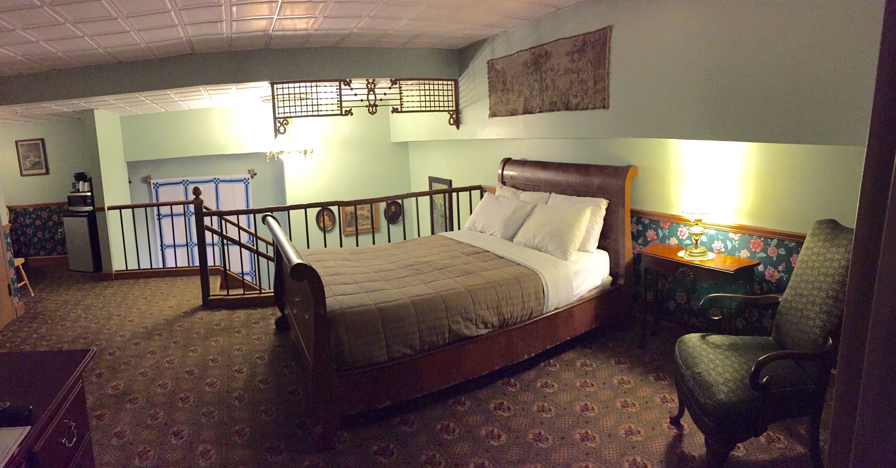 A bedroom with a bed, a chair, a desk, and a staircase.