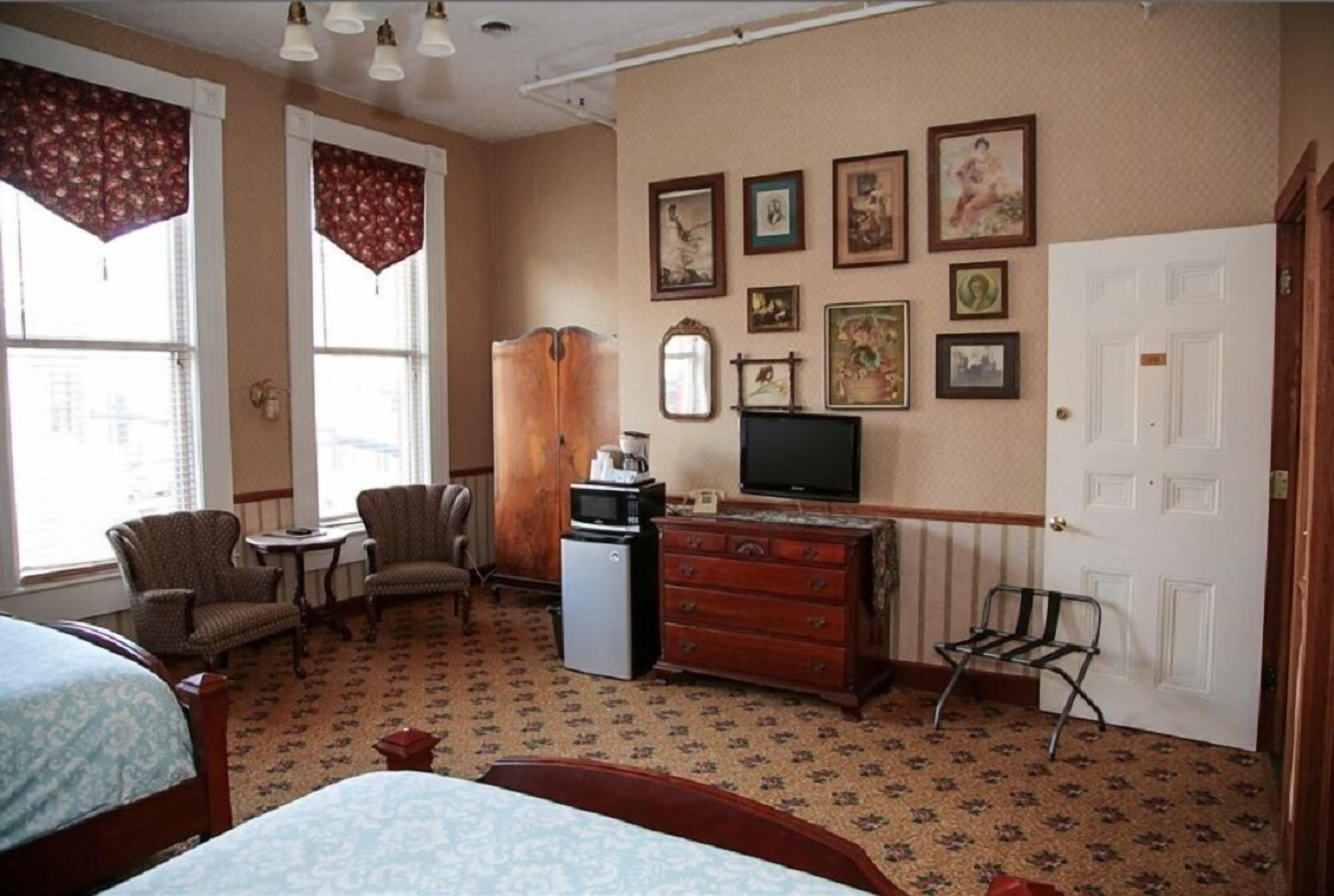 Habitación de hotel con cama, dos sillones, una mesita, cómoda, televisor y puerta.