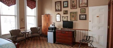 Habitación de hotel con cama, dos sillones, una mesita, cómoda, televisor y puerta.
