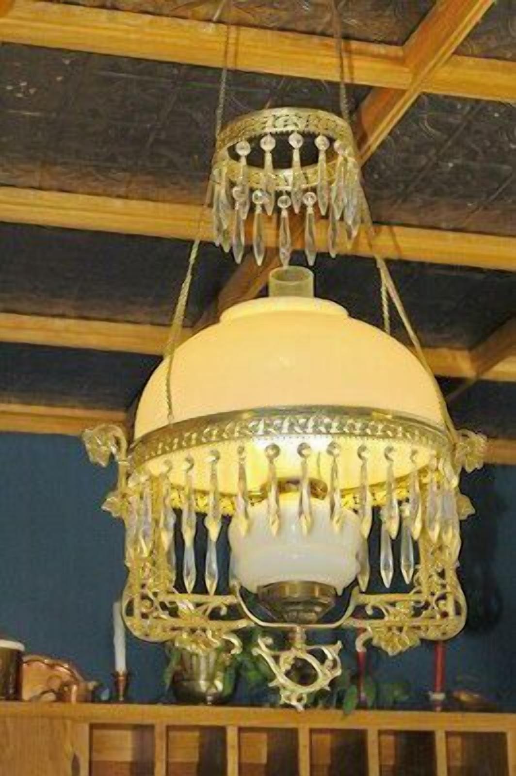 Un candelabro con ornamentación metálica detallada y una pantalla blanca, colgando del techo de madera.