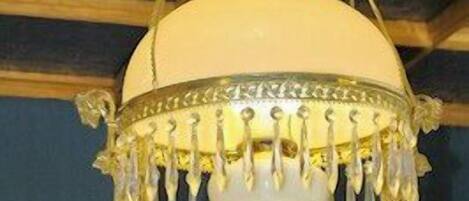 Un candelabro con ornamentación metálica detallada y una pantalla blanca, colgando del techo de madera.