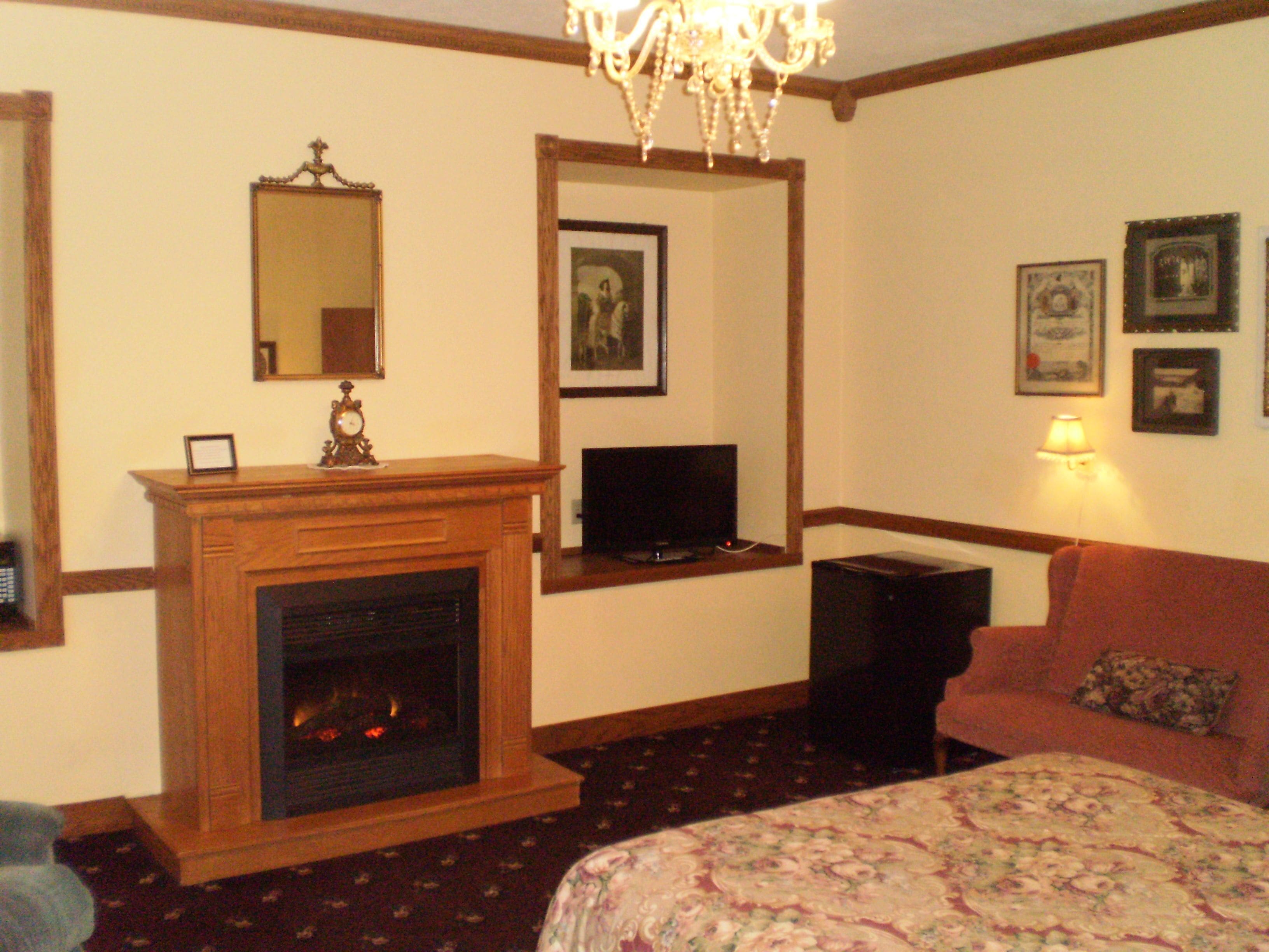 A hotel room with a fireplace, a television, a sofa, and framed pictures on the wall.