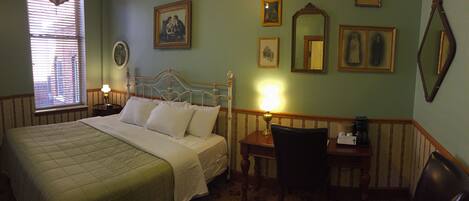 Habitación de hotel con cama, escritorio y silla. En la pared hay cuadros enmarcados y una ventana con persianas.