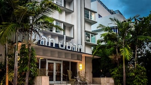 A hotel entrance with a sign reading "San Juan," featuring a modern design with glass doors, a staircase, and outdoor seating. - San Juan Hotel (Miami Beach)